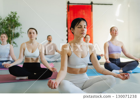 Yoga mindfulness meditation. Group of sporty people doing exercise in studio for class for yoga wellness mindfulness meditation. Men women practicing yoga sitting in lotus pose meditating relaxing Yoga mindfulness meditation. Group of sporty people doing exercise in studio for class for yoga wellness mindfulness meditation. Men women practicing yoga sitting in lotus pose meditating relaxing 130071238