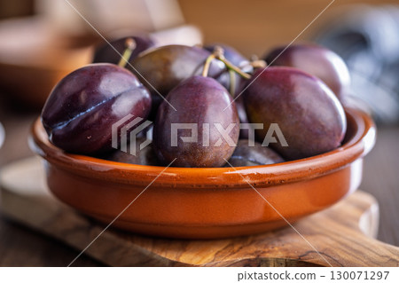 Ripe plums in bowl on wooden table. 130071297