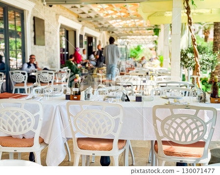 Tables set at an outdoor restaurant with guests in the background. Hospitality, leisure, and summer dining experience. Tables set at an outdoor restaurant with guests in the background. Hospitality, leisure, and summer dining experience. 130071477