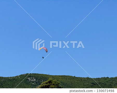 A paraglider flying high in the clear blue sky above the horizon. Freedom, adventure and extreme recreation in open aerial space. 130071498