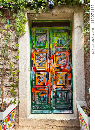 Painted colorful door on stone wall in narrow street. Urban creativity, cultural expression and artistic individuality in Mediterranean setting. Painted colorful door on stone wall in narrow street. Urban creativity, cultural expression and artistic individuality in Mediterranean setting. 130071525