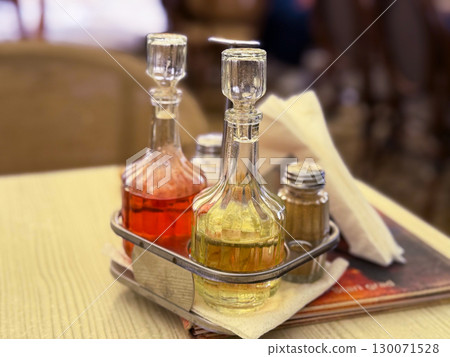 Glass bottles with oil, vinegar and spices on a cafe table. Culinary tradition, Mediterranean lifestyle and casual dining culture indoors. Glass bottles with oil, vinegar and spices on a cafe table. Culinary tradition, Mediterranean lifestyle and casual dining culture indoors. 130071528