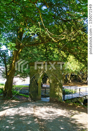 Stone arched gateway entrance to a beautiful garden in Ireland, under the shade of large trees. Stone arched gateway entrance to a beautiful garden in Ireland, under the shade of large trees. 130071549