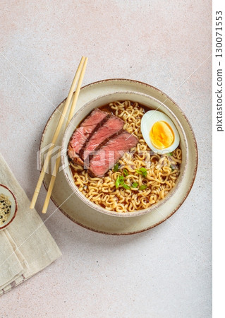 Ramen or asian style noodles soup with beef, egg and green onions in bowl on light beige background top view 130071553