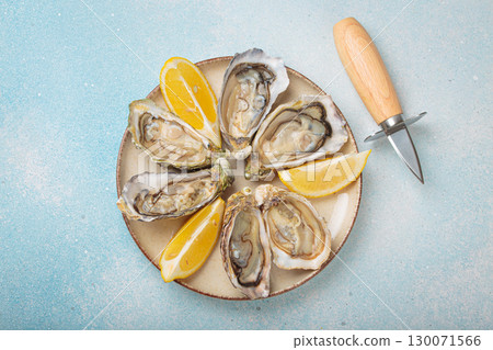 Fresh oysters with lemon wedges and oyster knife on plate top view 130071566