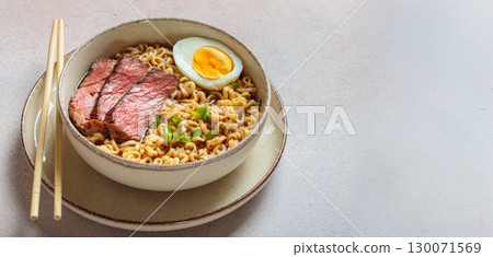 Ramen or asian style noodles soup with beef, egg and green onions in bowl on light beige background, space for text 130071569