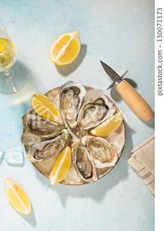 Fresh oysters with lemon and white wine on ice for a luxurious meal on sunny day, blue background Fresh oysters with lemon and white wine on ice for a luxurious meal on sunny day, blue background 130071573