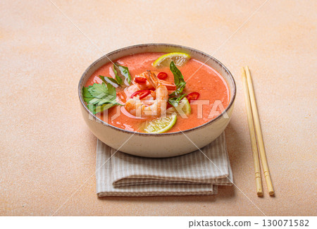 Traditional Thai soup tom yum soup with shrimp, lime, and herbs in bowl with chopsticks on light beige background 130071582