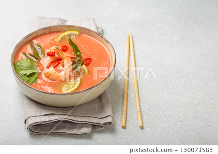 Traditional Thai soup tom yum soup with shrimp, lime, and herbs in bowl with chopsticks on light grey background, space for text Traditional Thai soup tom yum soup with shrimp, lime, and herbs in bowl with chopsticks on light grey background, space for text 130071583