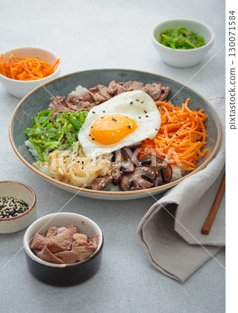 Traditional korean bibimbap with fried egg, beef and vegetables and other toppings on light background with chopsticks Traditional korean bibimbap with fried egg, beef and vegetables and other toppings on light background with chopsticks 130071584