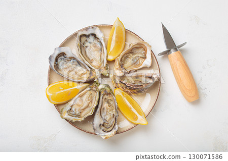 Fresh oysters with lemon wedges and oyster knife on plate top view 130071586
