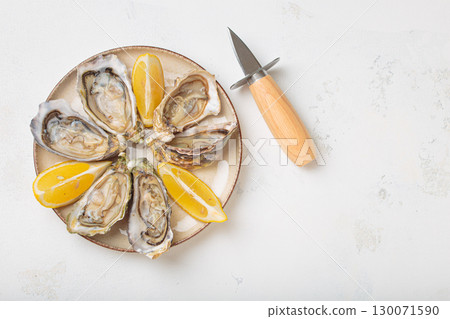 Fresh oysters with lemon wedges and oyster knife on plate top view, space for text 130071590