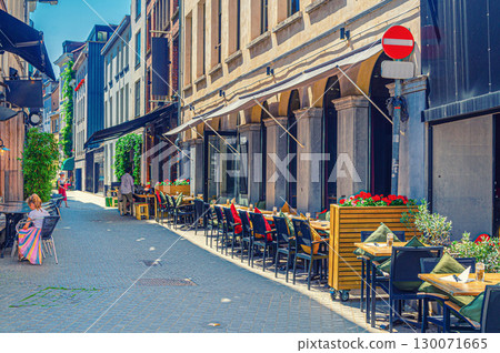 Street restaurant with tables and chairs on narrow street, road with paving stone, old buildings in Antwerp historical city center, street cafe in old town Antwerpen, Belgium Street restaurant with tables and chairs on narrow street, road with paving stone, old buildings in Antwerp historical city center, street cafe in old town Antwerpen, Belgium 130071665