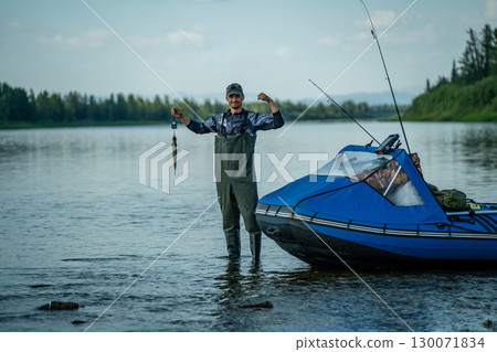 A satisfied fisherman holds fish on scales in a river 130071834