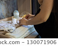 A pregnant woman lays out baby clothes and accessories on a changing table, preparing for childbirth and motherhood, showing love and care. A pregnant woman lovingly prepares a nursery. 130071906
