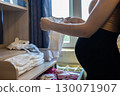 Pregnant woman keeps baby clothes, puts little things in a chest of drawers, prepares for childbirth and motherhood, creates a cozy nursery. Pregnant woman prepares for the arrival of a child. 130071907