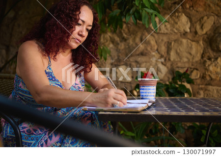 Woman Writing Outdoors on a Stone Patio with Tropical Plants in Background Woman Writing Outdoors on a Stone Patio with Tropical Plants in Background 130071997