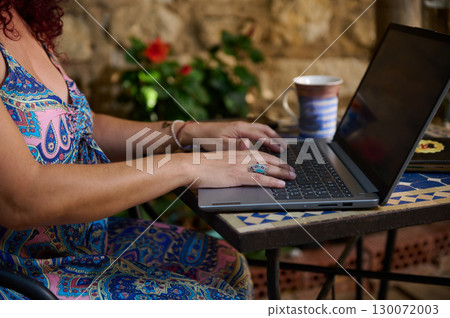 Woman Typing on Laptop at Outdoor Table with Coffee in Backyard 130072003