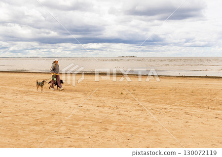 professional dog walker. person walks two pets on beach. dogs on leashes, woman is wearing hat. professional dog walker. person walks two pets on beach. dogs on leashes, woman is wearing hat. 130072119
