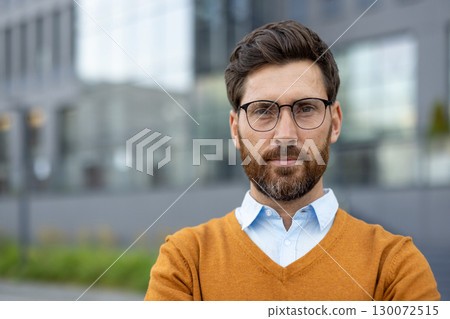 Confident man wearing glasses and a sweater, posing outdoors against a modern office background, demonstrating professionalism and poise, ideal for business, corporate, and leadership themes. 130072515