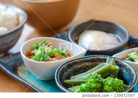 A Japanese-style breakfast set featuring rice, miso soup, natto, a soft-boiled egg, and a small bowl of vegetables 130072597