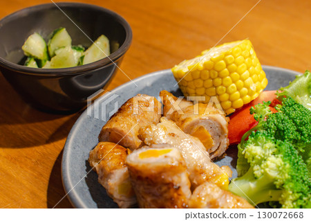 Dinner of pork wrapped in vegetables with a side dish of corn, vegetables, and cucumber 130072668
