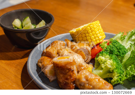 Dinner of pork wrapped in vegetables with a side dish of corn, vegetables, and cucumber Dinner of pork wrapped in vegetables with a side dish of corn, vegetables, and cucumber 130072669