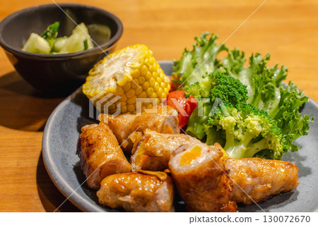 Dinner of pork wrapped in vegetables with a side dish of corn, vegetables, and cucumber Dinner of pork wrapped in vegetables with a side dish of corn, vegetables, and cucumber 130072670