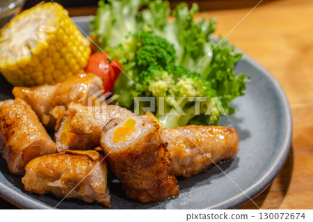 Dinner of pork wrapped in vegetables with a side dish of corn, vegetables, and cucumber 130072674