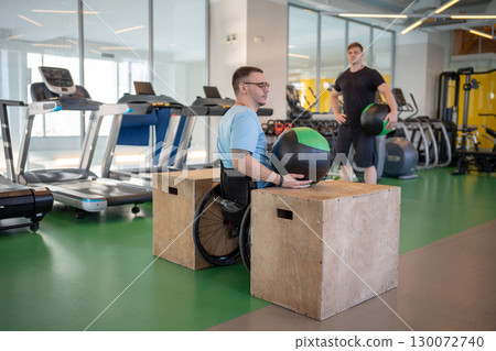 Rearview wheelchair athlete trains with personal coach. Injury rehab with weighted ball exercise Rearview wheelchair athlete trains with personal coach. Injury rehab with weighted ball exercise 130072740
