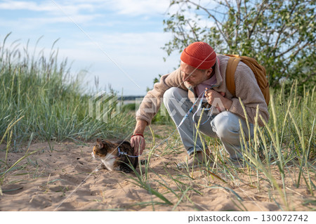 Thoughtful man soothing cat before beach adventure. Cautious pet uncomfortable in strange territory 130072742