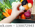 Close up of hand picking garlic from crate full of fresh organic vegetables including tomatoes, onions, carrots, cauliflower and broccoli 130072943