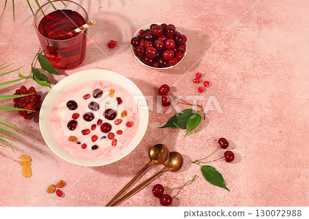 Fruit yogurt with cherry, pomegranate, raisins and fresh cow's cream for healthy eating on elegant table. Healthy breakfast with ingredients, kitchen background. Natural nutrition and diet concept. 130072988