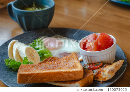 A Western-style breakfast plate with toast, fried eggs, bananas, tomatoes, and pizza. 130073023