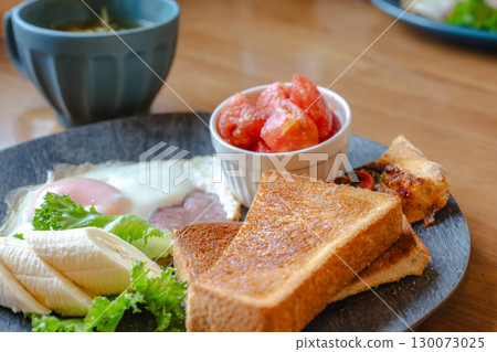 A Western-style breakfast plate with toast, fried eggs, bananas, tomatoes, and pizza. 130073025