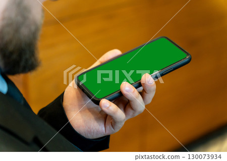 A businessman in a dark suit holds a smartphone horizontally during a meeting A businessman in a dark suit holds a smartphone horizontally during a meeting 130073934