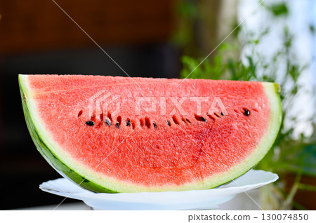 A sliced watermelon on a table in a room with an oscillating fan 130074850