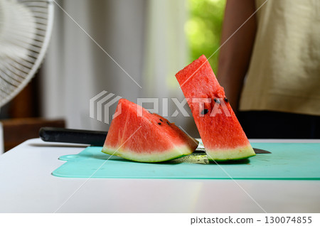 A sliced watermelon on a table in a room with an oscillating fan 130074855