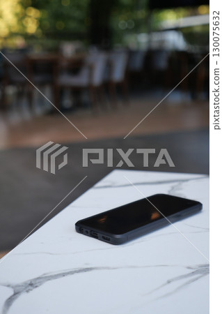 Black smartphone resting on marble table in restaurant. lost smart phone concept Black smartphone resting on marble table in restaurant. lost smart phone concept 130075632