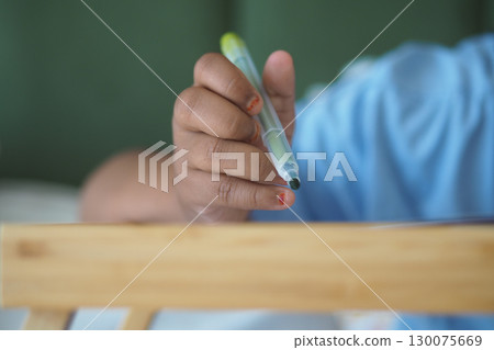 Child holding a pen while drawing on a wooden table Child holding a pen while drawing on a wooden table 130075669