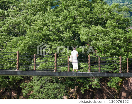 一位女遊客正穿越夏季熱門旅遊景點白川鄉的出合橋。 一位女遊客正穿越夏季熱門旅遊景點白川鄉的出合橋。 130076162
