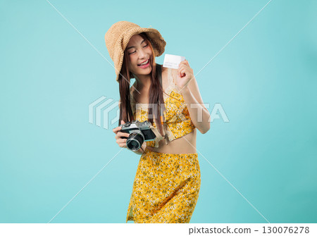 Happy asian woman, credit card, travel camera in hand, she holds bank card for online payment, floral outfit and hat ready to make another payment, enjoying vacation, isolated studio blue background 130076278