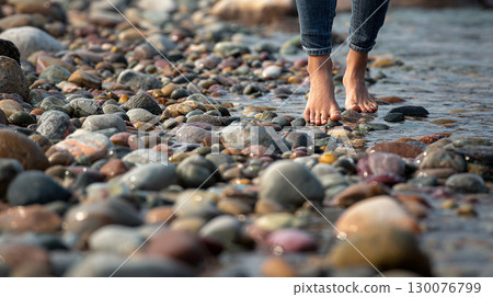 Barefoot woman walking on pebble beach under clear blue sky by the sea 130076799