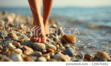 Barefoot woman walking on pebble beach under clear blue sky by the sea 130076802
