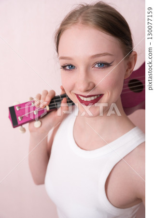 Young female musician holding ukulele by neck and slinging musical instrument over shoulder, she's feeling inspired. Beautiful woman looking camera with smile, positive attitude and happy expression 130077159