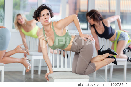 Woman sitting on knees on chair performs lap dance. Female students repeat erotic movements 130078541