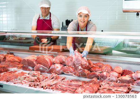 Positive young saleswoman vendor in apron and disposable gloves shows meat tenderloin Positive young saleswoman vendor in apron and disposable gloves shows meat tenderloin 130078563