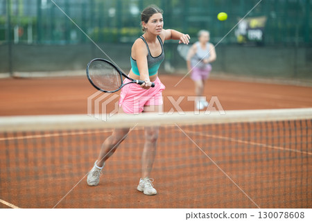 Focused girl playing doubles tennis on outdoor court 130078608