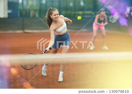 Fit girl engrossed in doubles tennis game on clay court 130078610