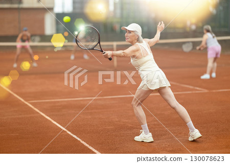 Elderly woman engrossed in tennis game on clay court Elderly woman engrossed in tennis game on clay court 130078623